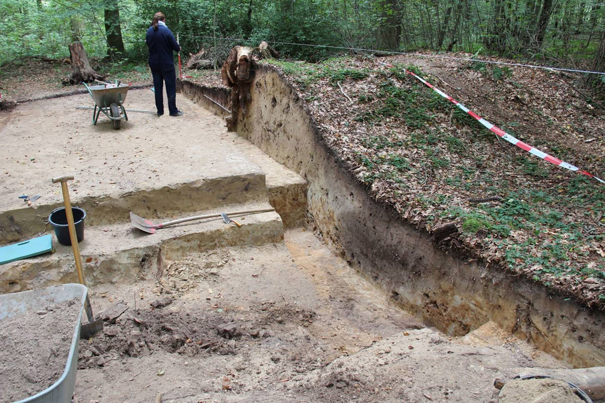 Der Wallschnitt mit dunkler verwaschener Grabenverfärbung im Vordergrund. Zeichnung des Wallprofils durch W. Köhne-Wulf, NLD.